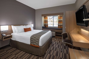 Une chambre d’hôtel comprenant un lit, une table de chevet avec un téléphone, un bureau avec une chaise, un téléviseur fixé au mur et une fenêtre avec des rideaux.