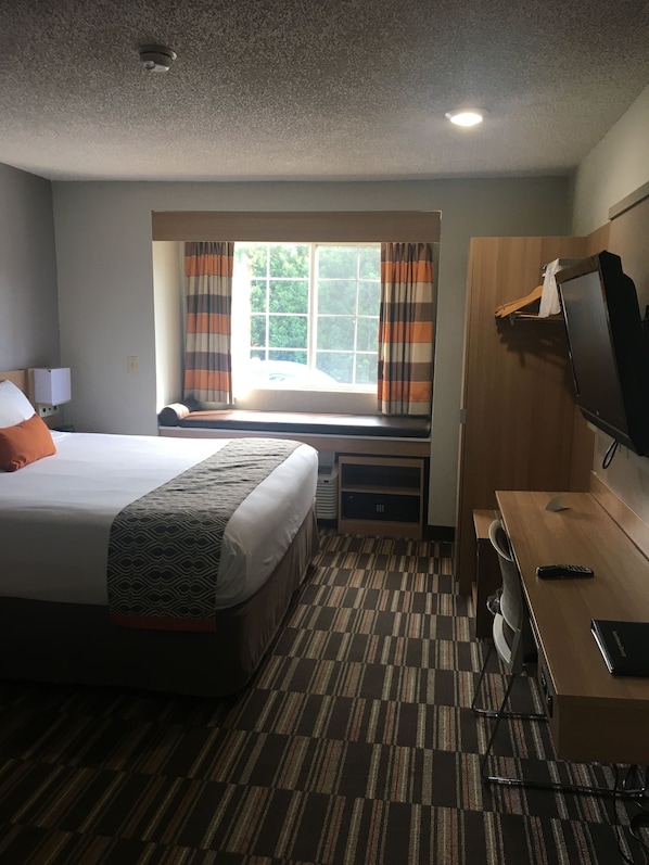 Une chambre d’hôtel avec un lit, un bureau, une télévision et une fenêtre avec des rideaux.