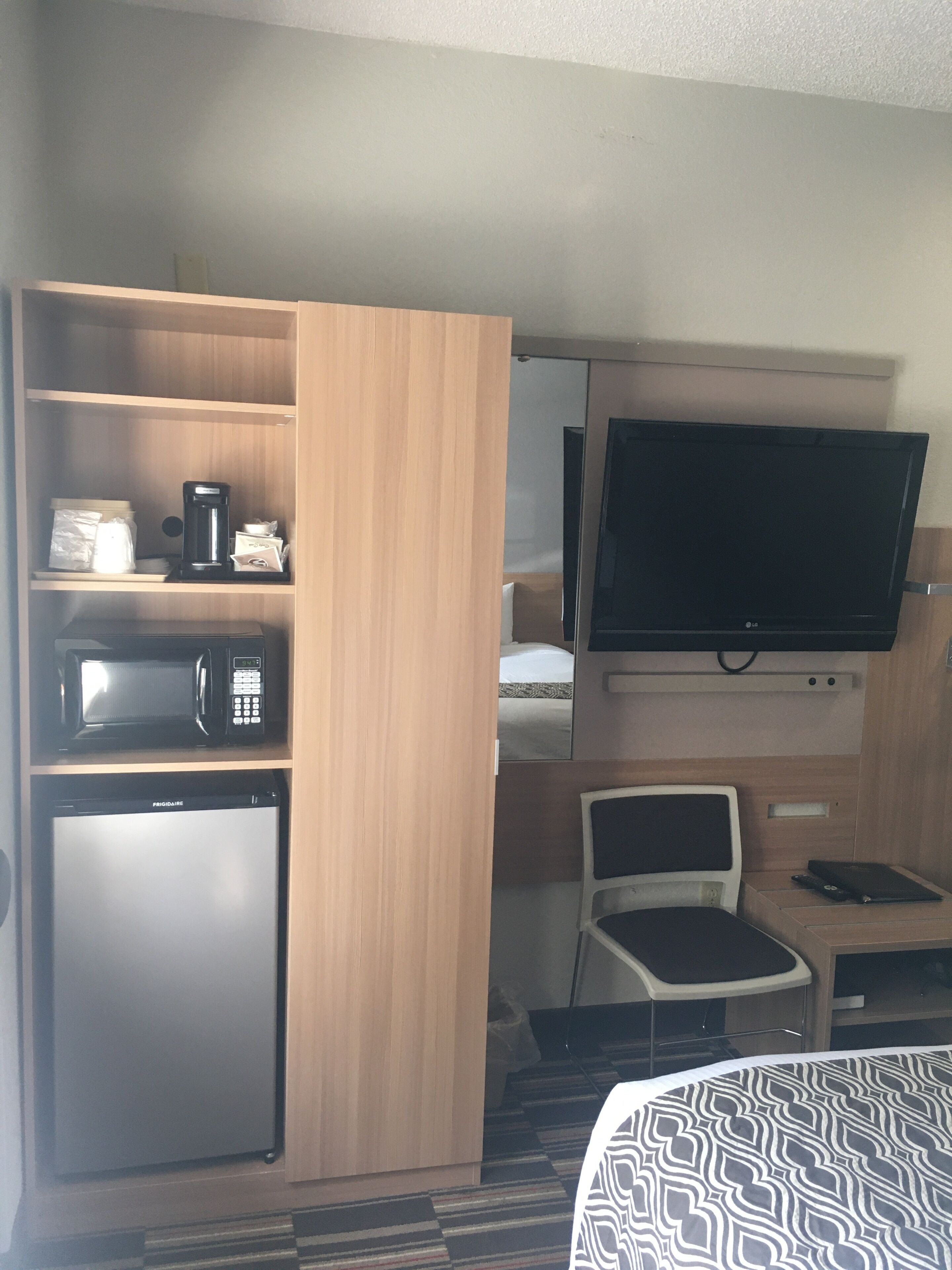 A compact hotel room with a kitchenette, a flat-screen TV, a bed, and a small seating area.