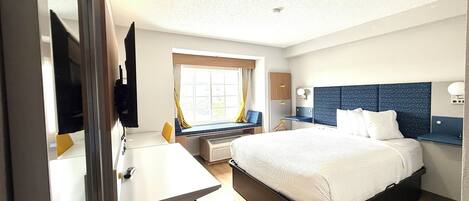 A hotel room with a bed, a desk, a chair, a TV, and a window with curtains.
