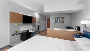 A modern hotel room with a bed, a desk, a flat-screen TV, a bathroom with a sink and mirror, and a painting on the wall. - Microtel Inn & Suites by Wyndham Sioux Falls (Sioux Falls)