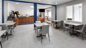 A modern dining area with tables and chairs, a kitchen in the background, and a large window providing natural light. - Microtel Inn & Suites by Wyndham Sioux Falls (Sioux Falls)