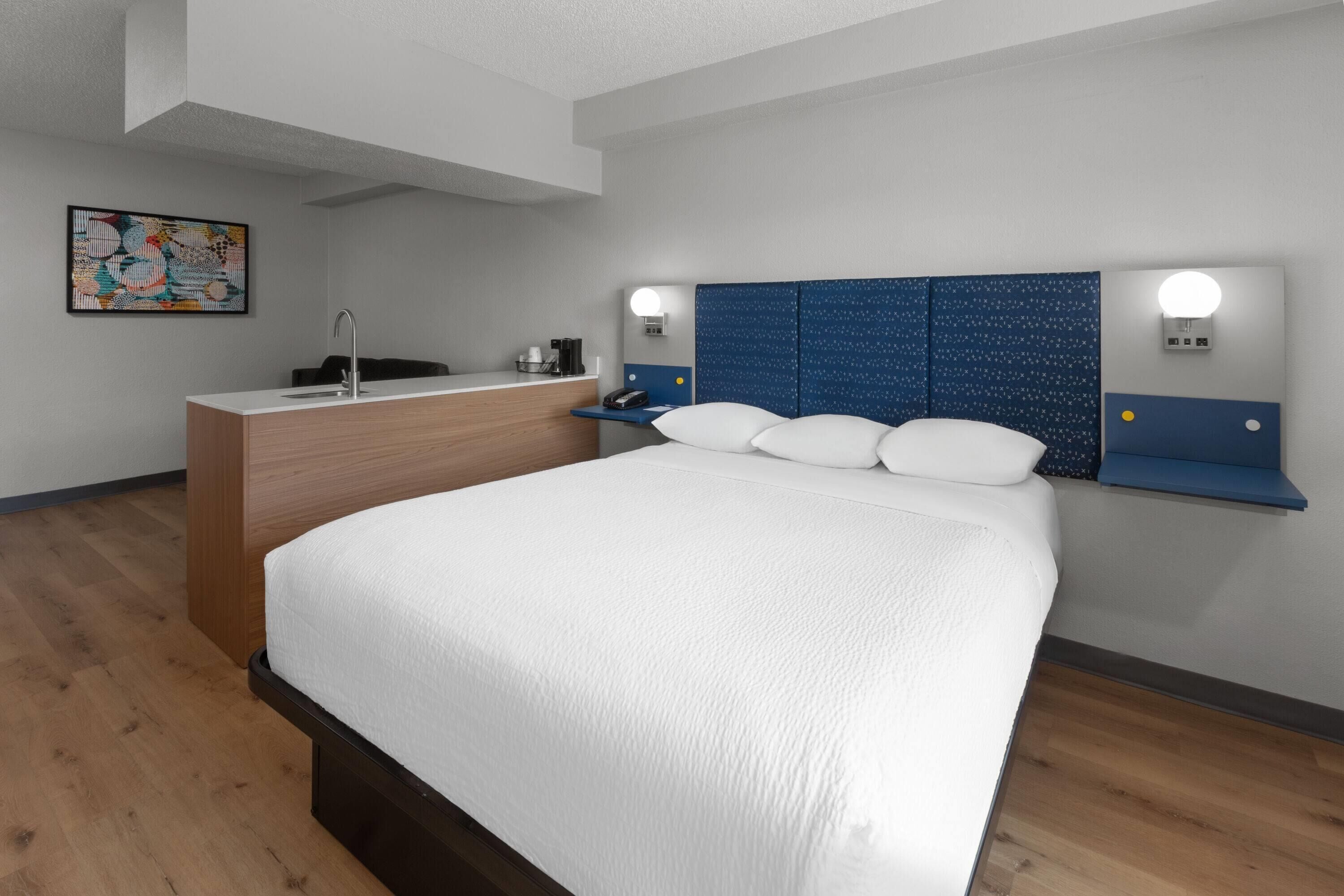 Una habitación de hotel moderna con una cama grande, un escritorio de madera y un cabecero azul con iluminación.