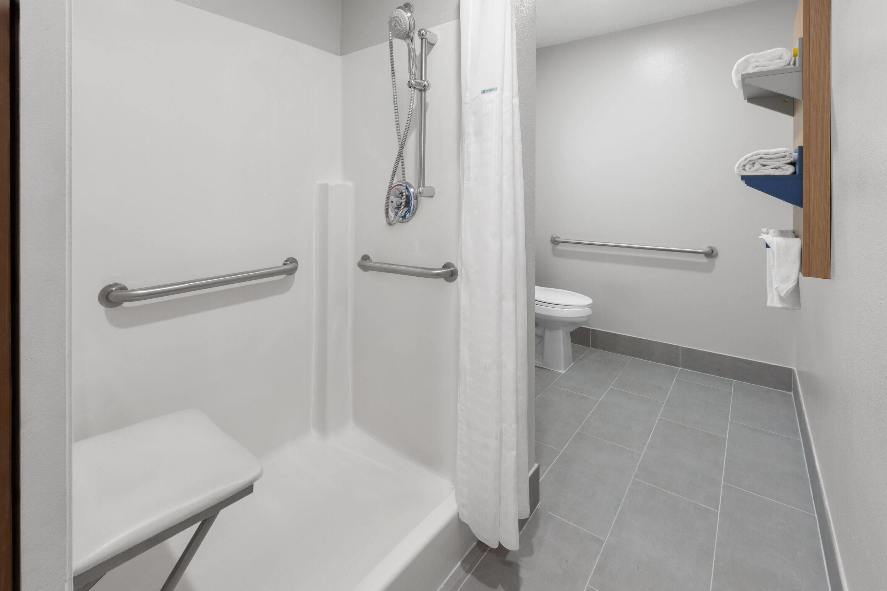 A bathroom with a shower, toilet, and a small bench.