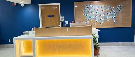 A reception desk with a wooden finish, a digital screen, and a sign indicating an office.