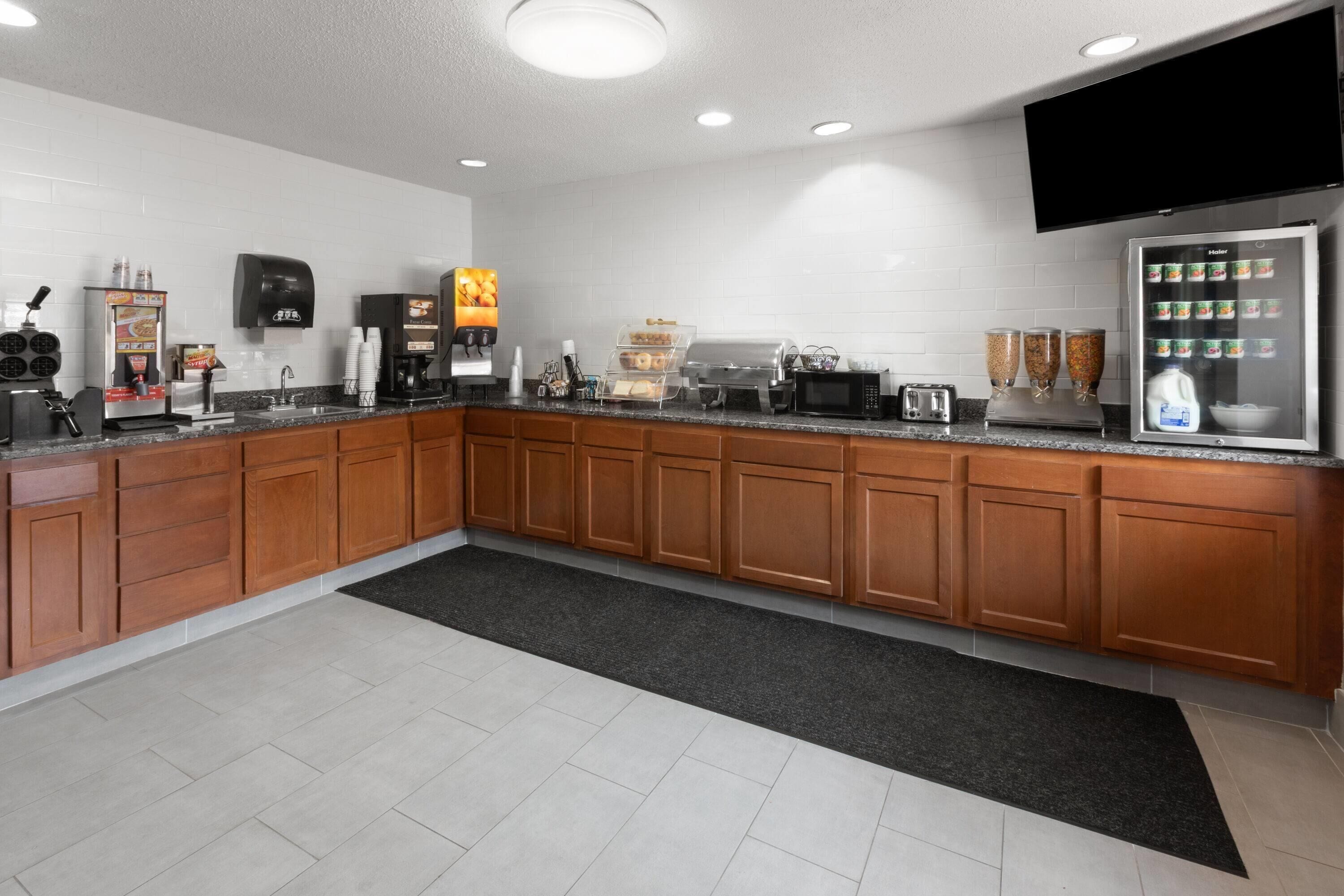 A modern kitchen with wooden cabinets, a stainless steel refrigerator, a coffee machine, and a microwave.