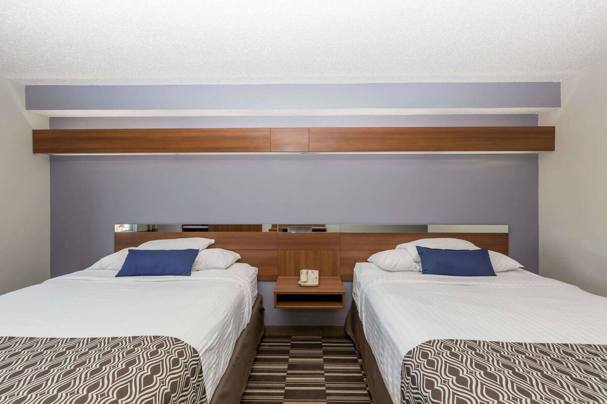 A hotel room with two beds, a nightstand, and a headboard.