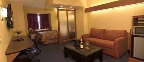 Una habitación de hotel con cama, un sofá, una mesita con una vela, un escritorio con una silla y una kitchenette.