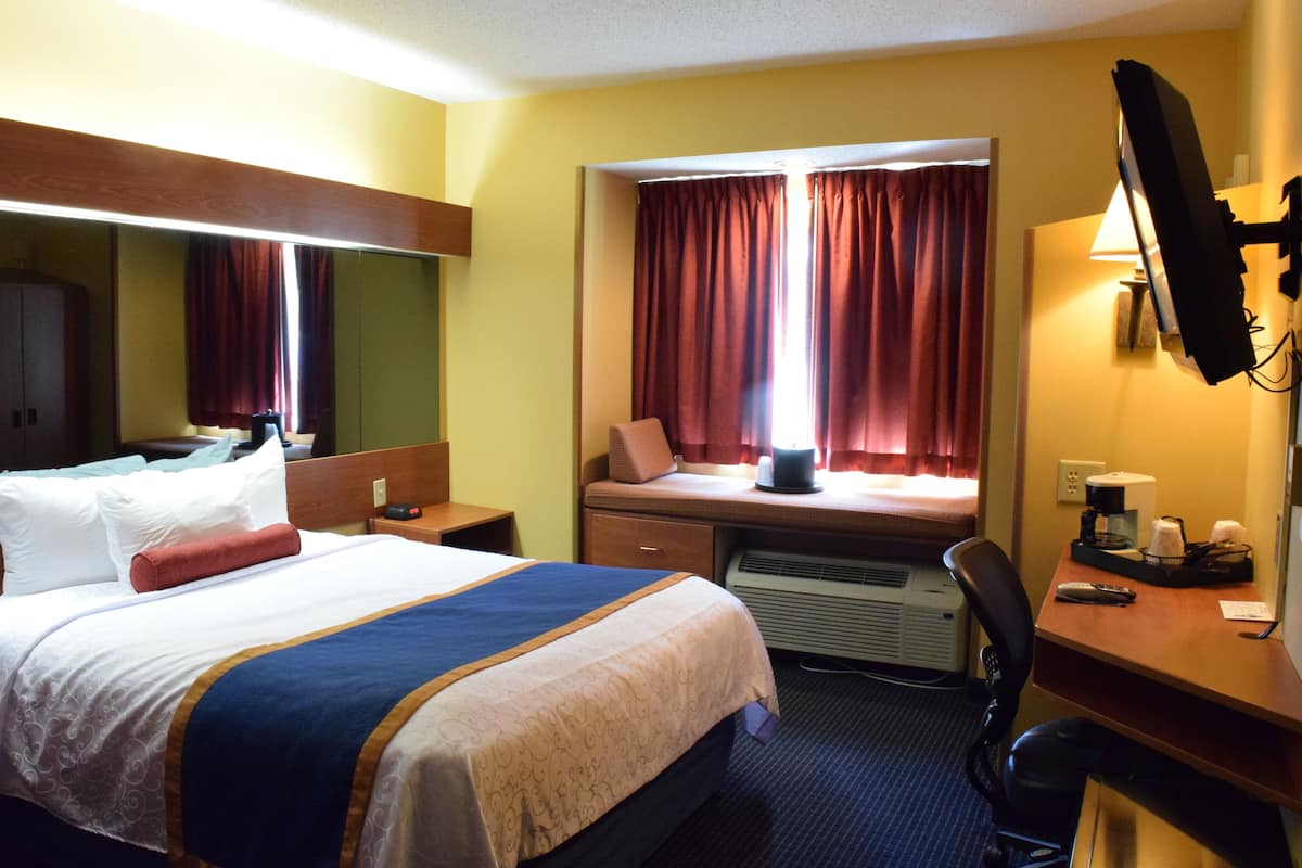 A hotel room with a bed, desk, chair, and a large mirror.