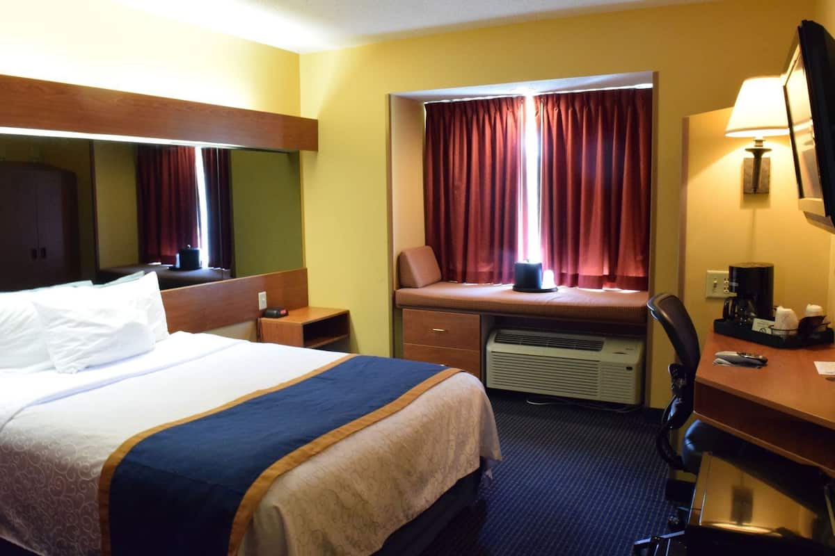 A hotel room with a bed, desk, chair, window with curtains, and a heater.