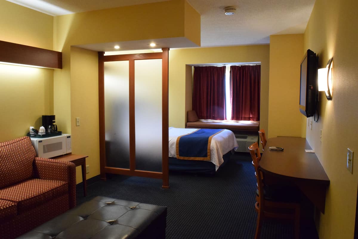 A hotel room with a bed, a desk, a chair, a couch, and a television.