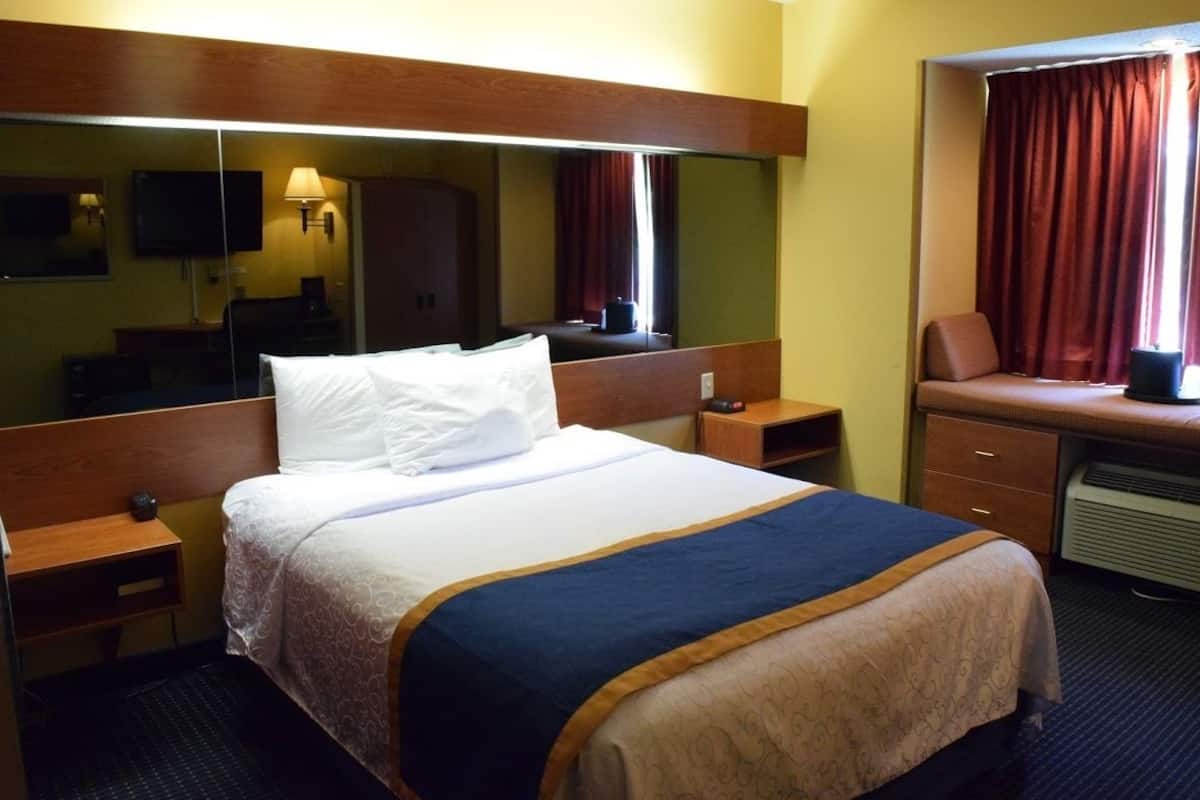 A hotel room with a large bed, a desk with a chair, a mirror, and a television.