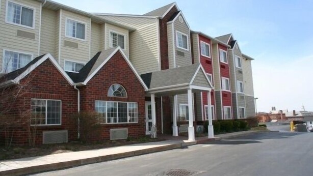 A multi-story residential building with a mix of brick and siding exteriors, a covered entryway, and a clear sky. - Inn at the Finger Lakes (Auburn)