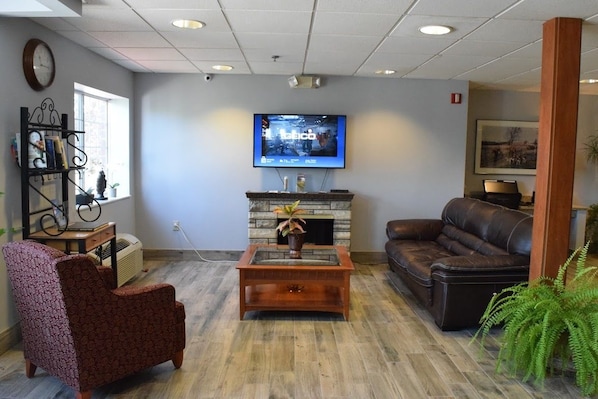 A living room with a fireplace, a television, a sofa, and a chair. - Inn at the Finger Lakes (Auburn)