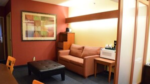 A compact room with a sofa, a small table, a microwave, and a framed artwork on the wall. - Inn at the Finger Lakes (Auburn)