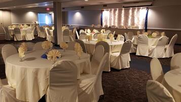 A banquet hall with round tables covered in white tablecloths, each set with white chairs and centerpieces.