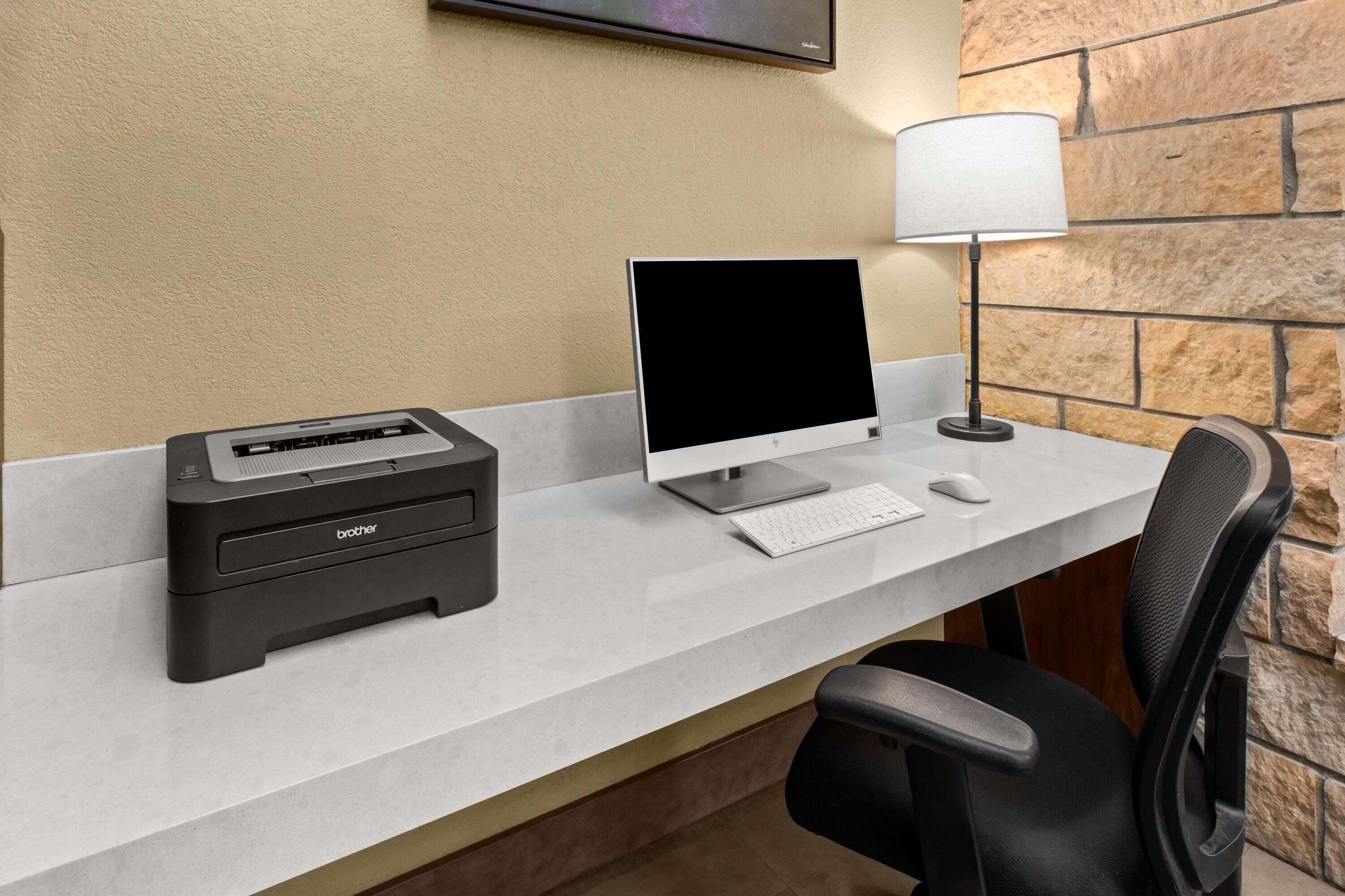 A desk with a desktop computer, a printer, a lamp, and a chair.