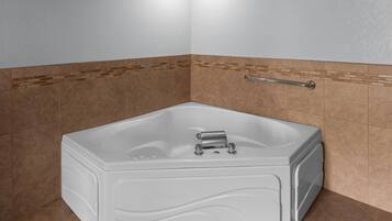 A corner bathroom with a white bathtub, a handrail, and brown tiled walls.