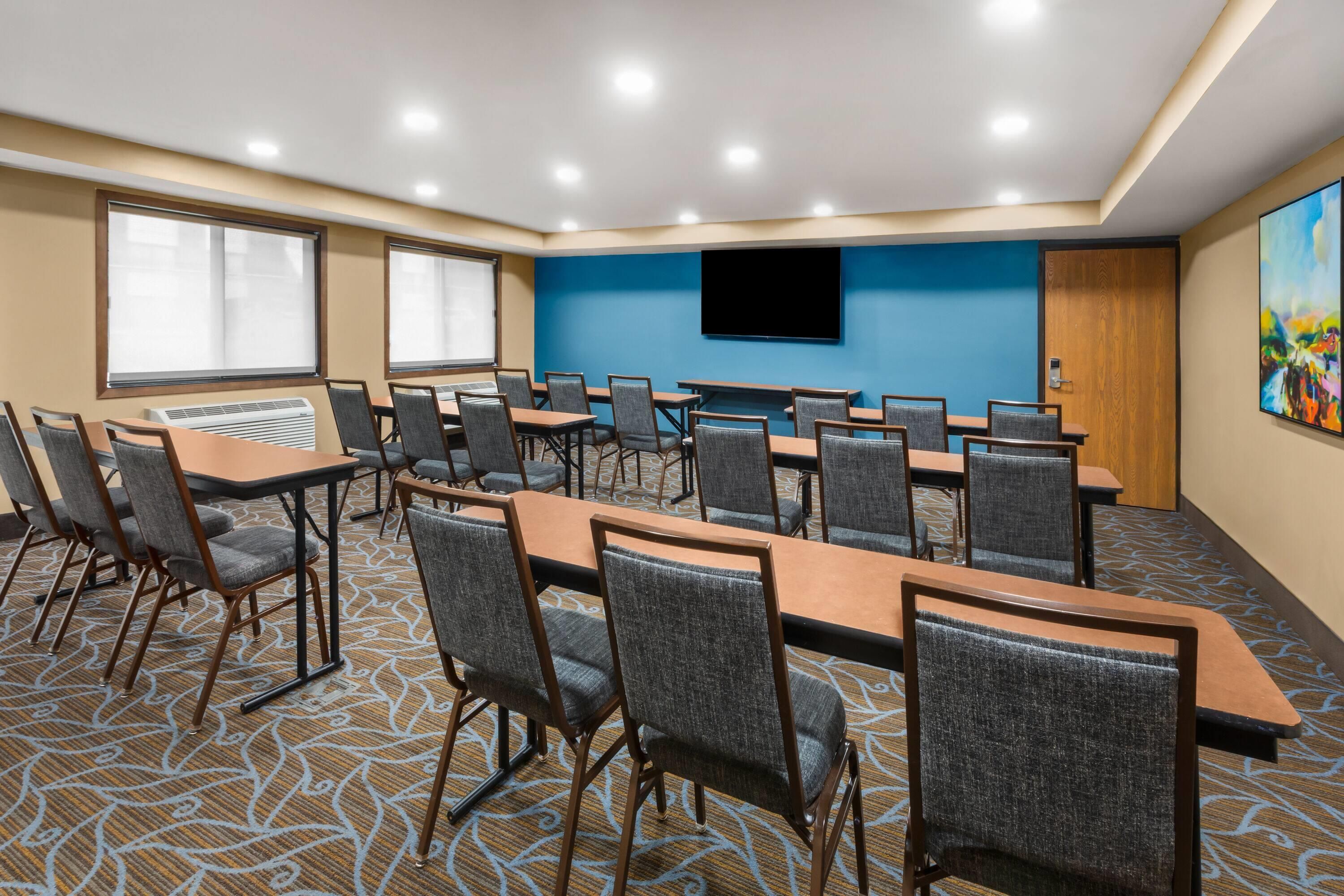 A conference room with multiple tables and chairs, a large flat-screen TV mounted on the wall, and a patterned carpet.