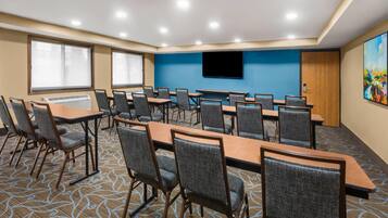 A conference room with multiple tables and chairs, a large flat-screen TV mounted on the wall, and a patterned carpet.