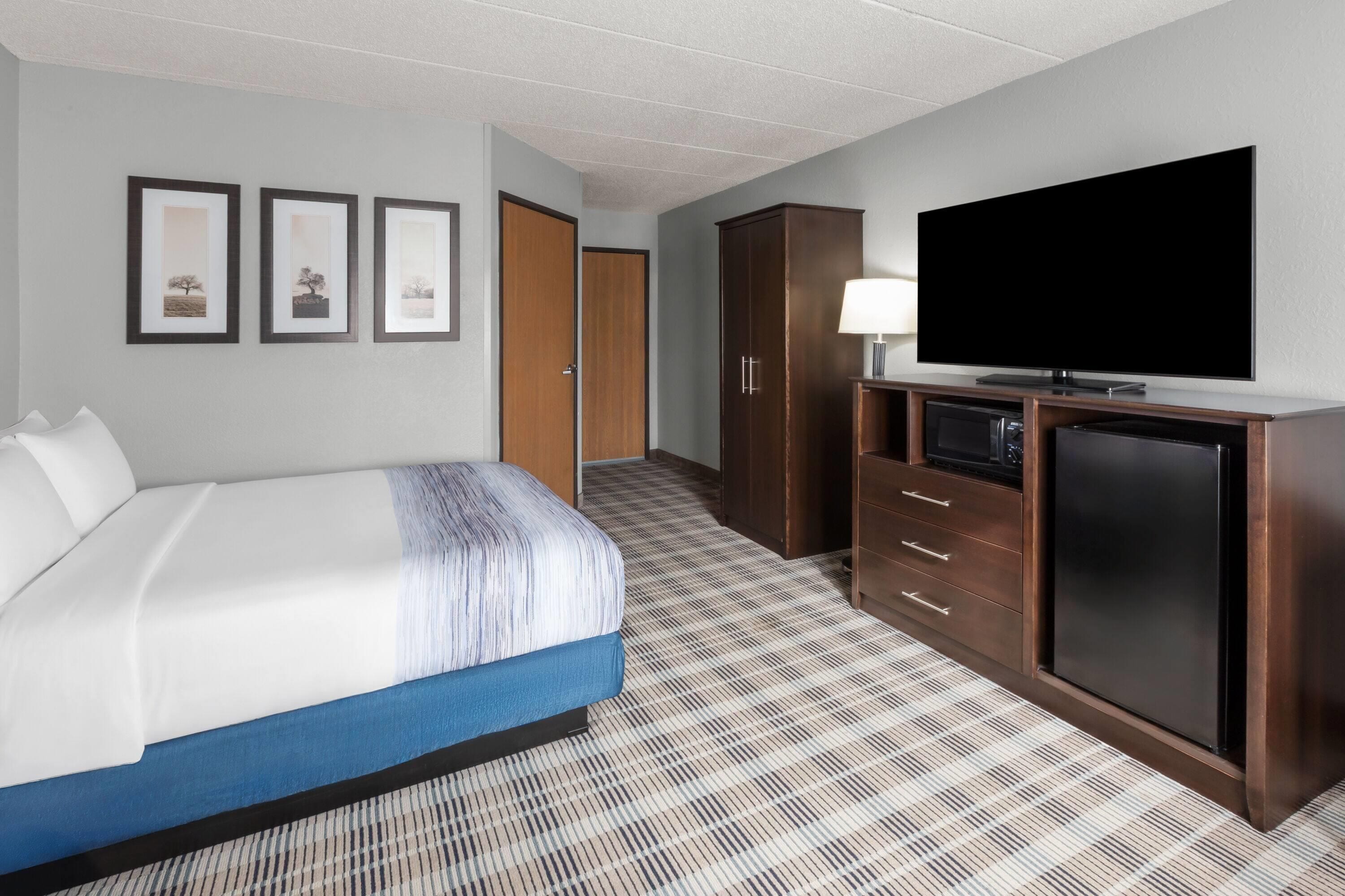 A hotel room with a bed, a television, a desk with a lamp, and a wardrobe.