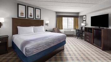 A hotel room with a large bed, a desk with a chair, a television, and framed pictures on the wall.