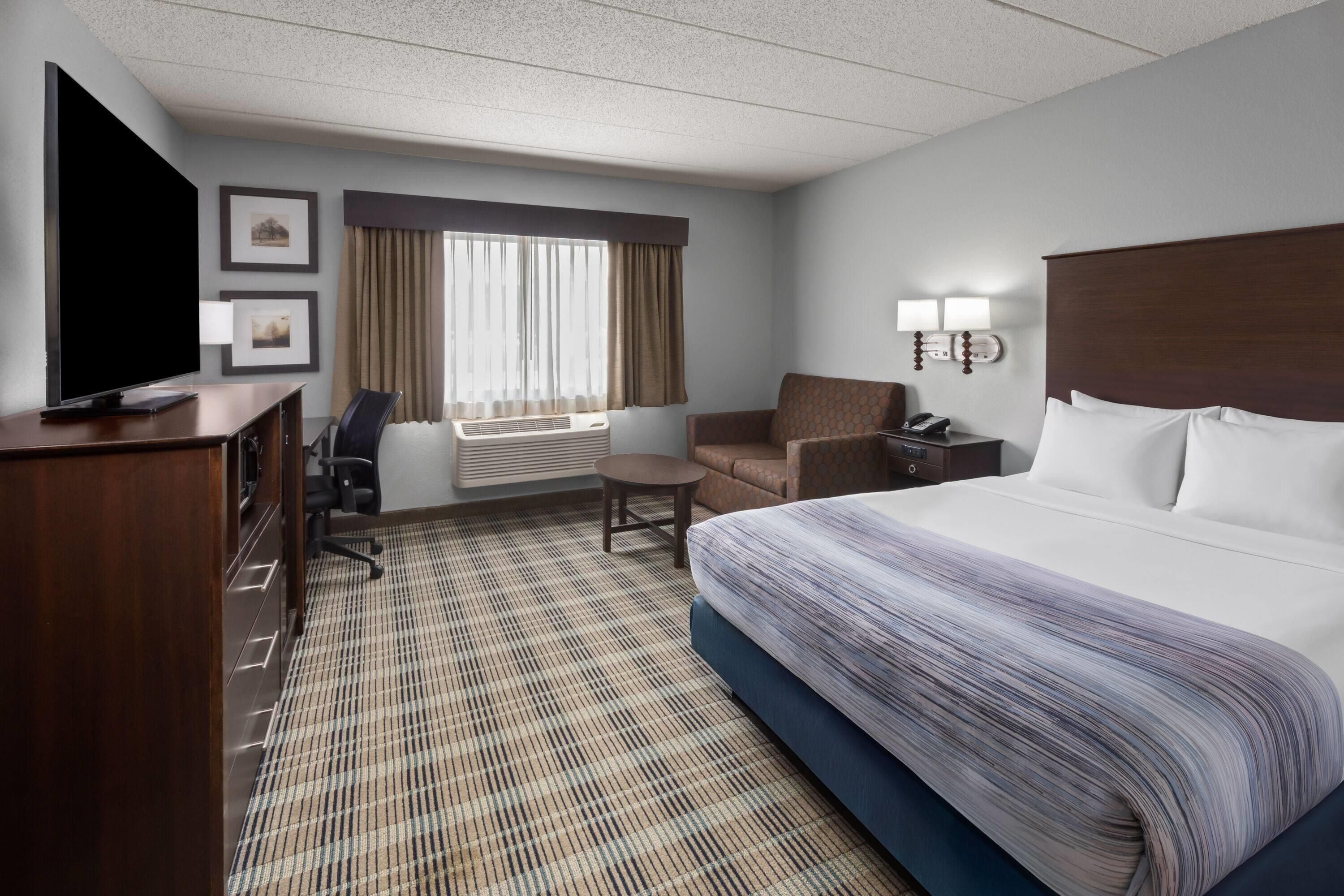 A hotel room with a bed, a desk, a chair, a TV, and a window with curtains.