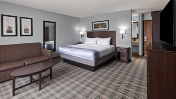 Habitación de hotel con cama, sofá, escritorio, televisión y baño visible a través de una puerta abierta.