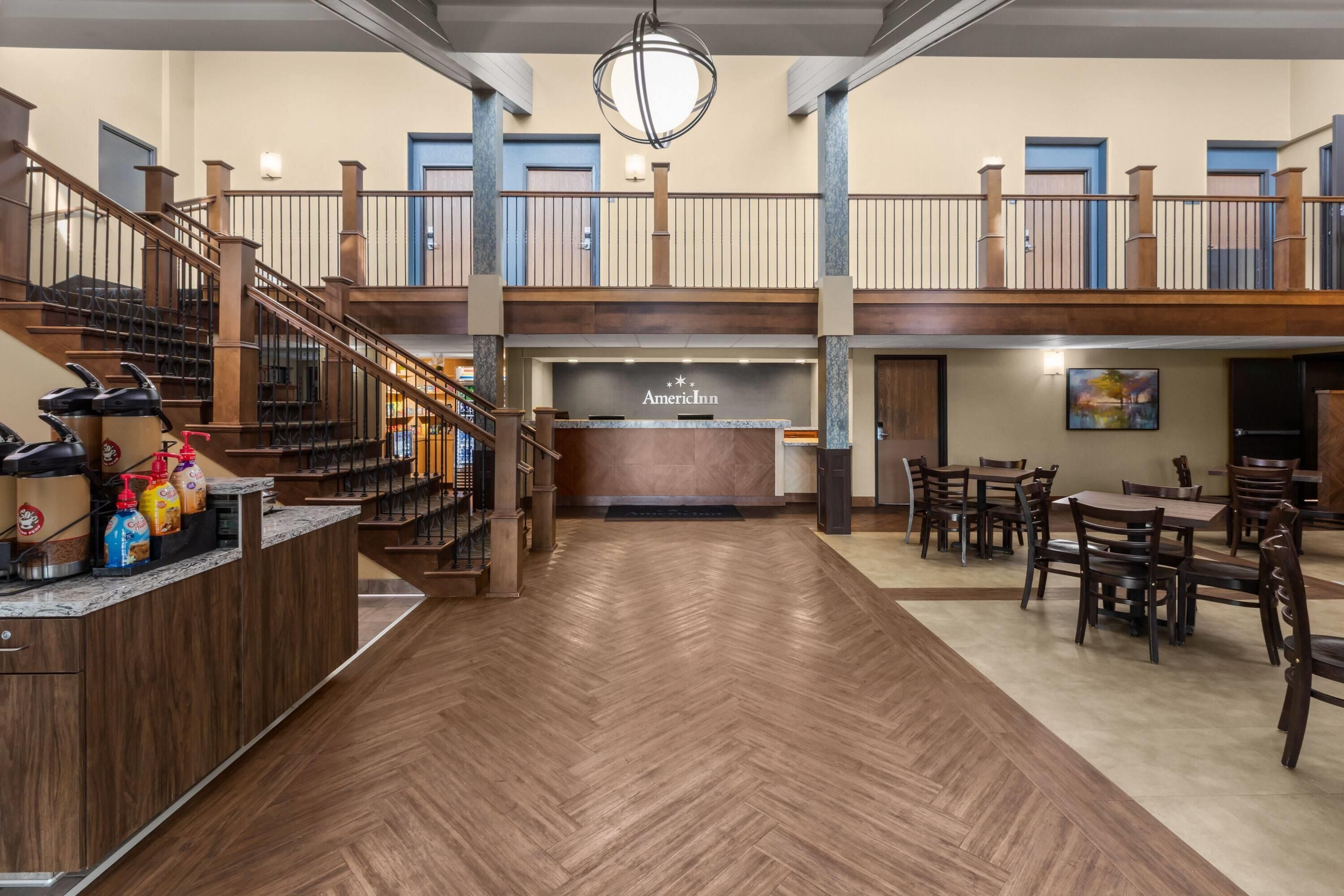 A hotel lobby with a reception desk, a coffee station, and a seating area with tables and chairs.