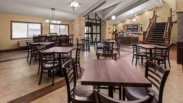 A spacious dining area with multiple tables and chairs, a kitchen area, and a staircase.
