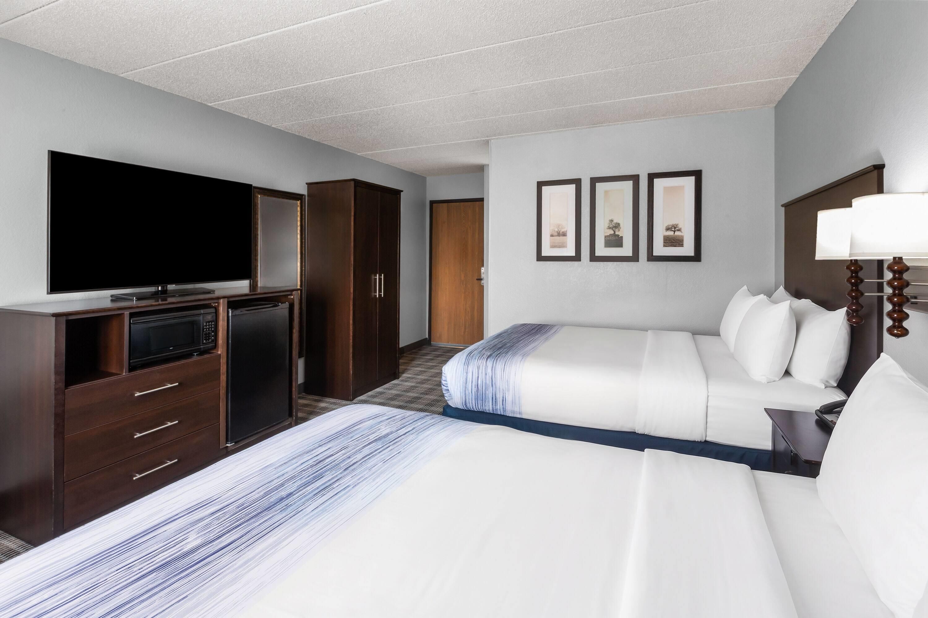 A hotel room with a flat-screen TV, a wardrobe, a bed with white bedding, a bedside table with a lamp, and three framed pictures on the wall.