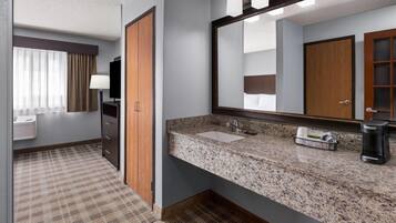 A hotel bathroom with a granite countertop, a sink, a mirror, and a coffee maker.