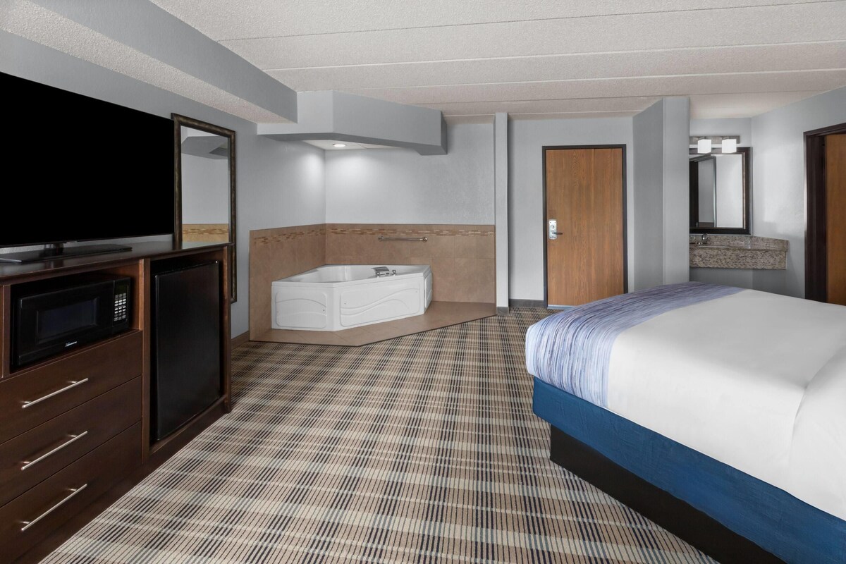 A hotel room with a bed, a television, a bathroom with a bathtub, and a mirror.