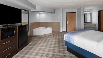 Quarto de hotel com cama, televisão, banheiro com banheira e espelho.