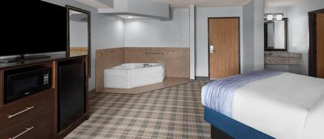 Habitación de hotel con cama, televisor, baño con bañera y espejo.