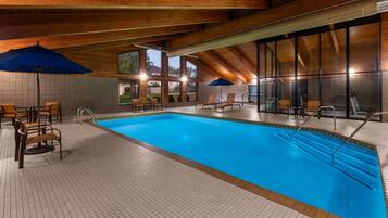 An indoor swimming pool with tiled flooring, wooden ceiling beams, and multiple lounge chairs.