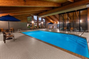 Una piscina interior con suelo de baldosas, vigas de madera en el techo y varias sillas de descanso.