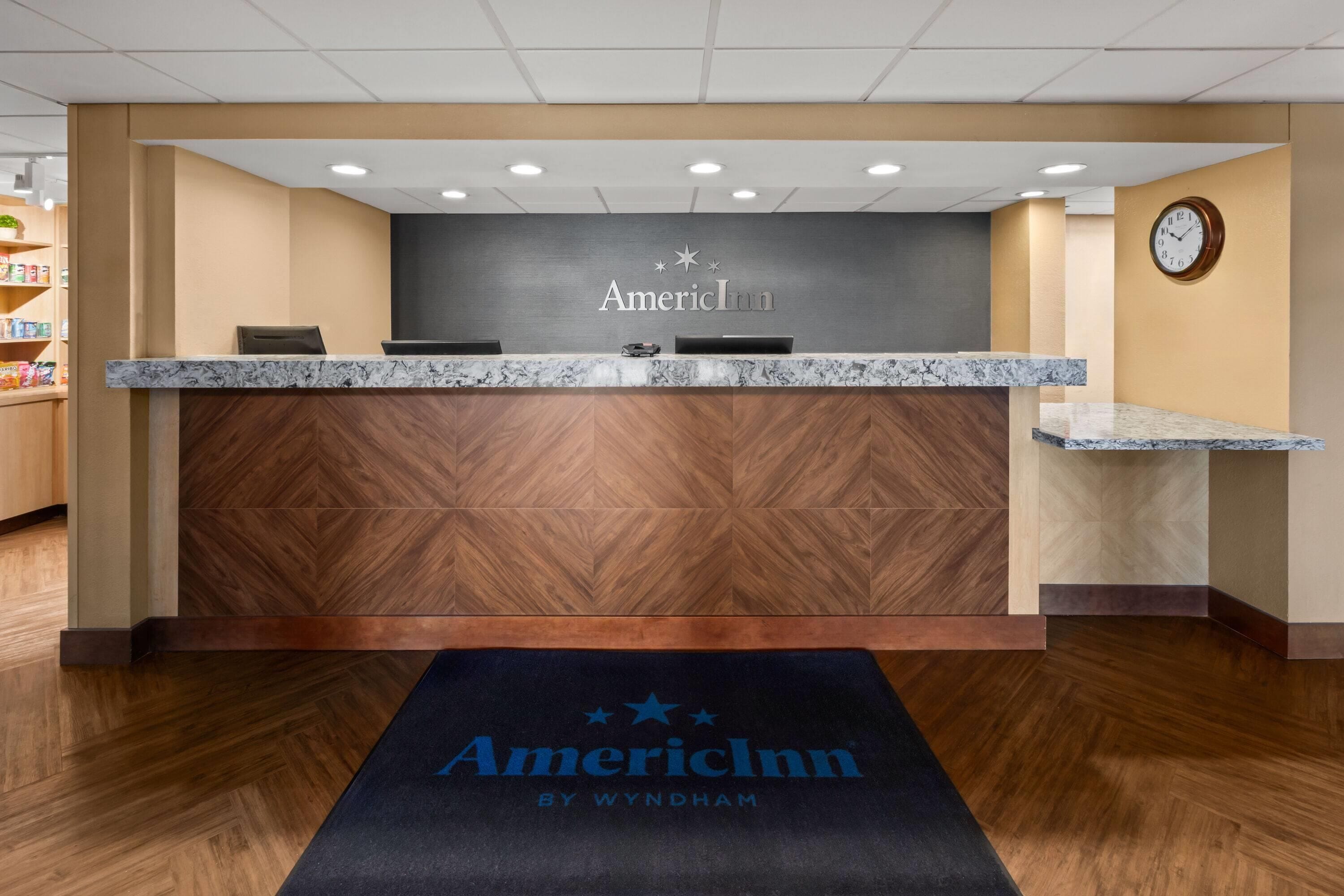 A reception desk with a marble top, a clock on the wall, and a carpet with the hotel name.