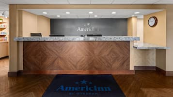A reception desk with a marble top, a clock on the wall, and a carpet with the hotel name.