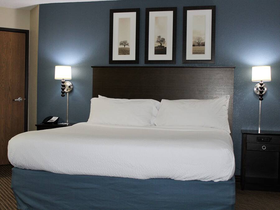 A hotel room with a large bed, two bedside tables with lamps, a wooden door, and three framed pictures on the wall.