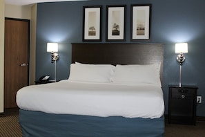 A hotel room with a large bed, two bedside tables with lamps, a wooden door, and three framed pictures on the wall. - AmericInn by Wyndham Mankato Event Center (Mankato)