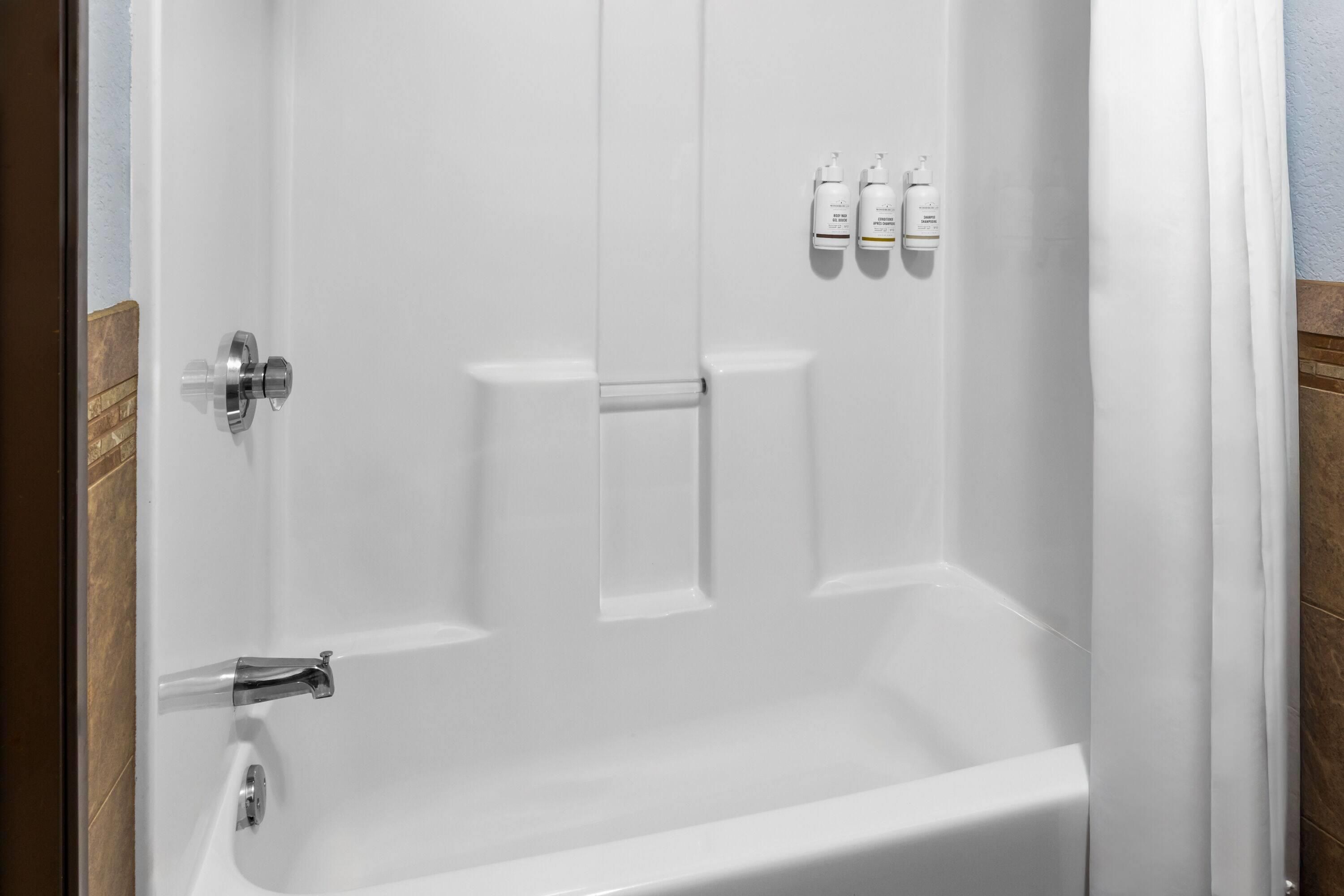 A white bathtub with a shower curtain, a faucet, and three bottles of shampoo and conditioner on the wall.