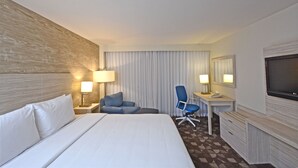 Una habitación de hotel con una cama grande, un escritorio con silla, un televisor y dos lámparas.
