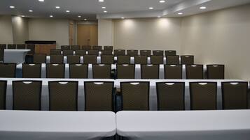 A conference room with rows of chairs and tables, a podium, and a door labeled 'SALIDA'.