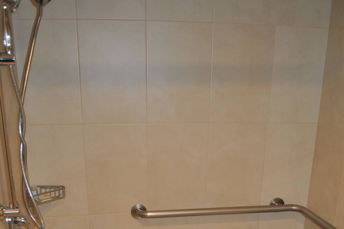 A shower area with a grab bar and a white shower chair.