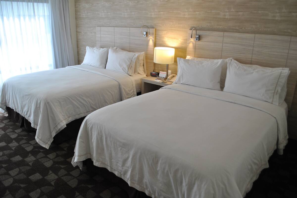 A hotel room with two beds, a nightstand with a lamp, and a patterned floor.