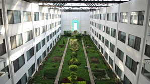 Un edificio de varios pisos con un patio central que presenta una distribución simétrica de jardín, una ventana de arco central y una serie de ventanas en cada planta.