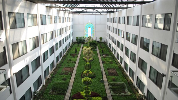 Un edificio de varios pisos con un patio central que presenta una distribución simétrica de jardín, una ventana de arco central y una serie de ventanas en cada planta.