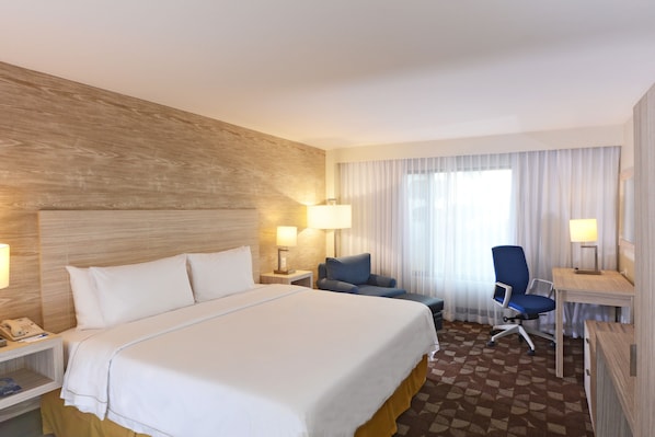 Una habitación de hotel con una cama grande, dos sillones, un escritorio y un teléfono sobre la mesita de noche.