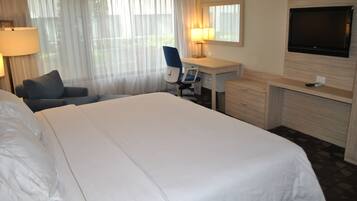 A hotel room with a large bed, a desk, a chair, a TV, and a window with curtains.